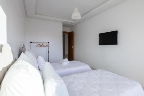 a bedroom with two white beds and a flat screen tv at Harhoura Val d'Or Grand Appart in Temara