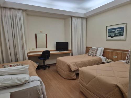 a hotel room with two beds and a desk at Nikkey Palace Hotel in Sao Paulo