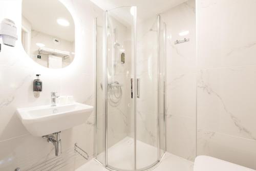 a white bathroom with a shower and a sink at Hôtel Restaurant Le Relays du Chasteau - Logis Hôtel in Brousse-le-Château