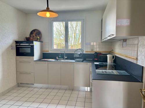 une cuisine avec des armoires blanches, un évier et une fenêtre dans l'établissement L'Ozormo - Climatisée - Maison - Jardin, à Amboise