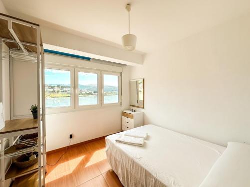 a white bedroom with a bed and a window at Apartamento Saica by ALÔGA in Corcubión