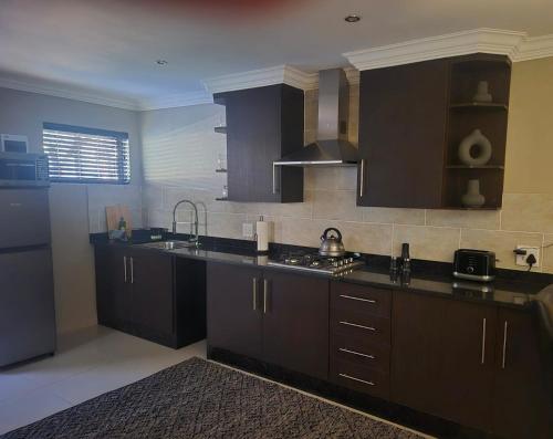 a kitchen with dark brown cabinets and a sink at Hornbill Self Catering Cottages Muldersdrift in Krugersdorp