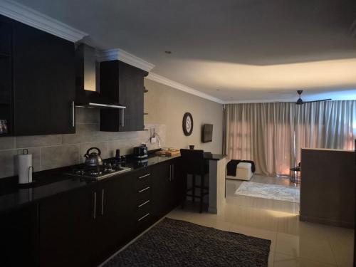 a kitchen with black cabinets and a living room at Hornbill Self Catering Cottages Muldersdrift in Krugersdorp