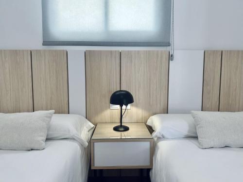 two beds with a lamp on a table between them at Apartamentos Turísticos Santo Rostro in Chipiona