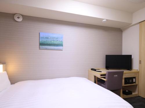 a bedroom with a bed and a desk with a television at Dormy Inn Sapporo Annex in Sapporo