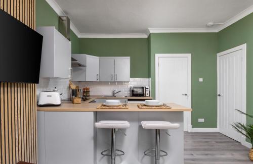 a kitchen with green walls and a counter with stools at Ochill View Apartment by Stirling Train Station in Stirling