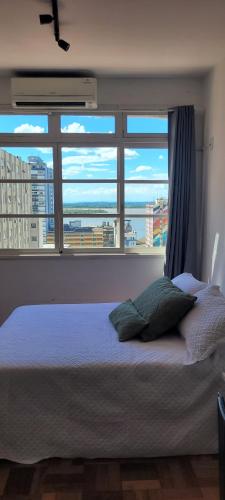 a bed in a bedroom with a large window at 13 andar, Studio, Centro, vista incrível Guaíba in Porto Alegre