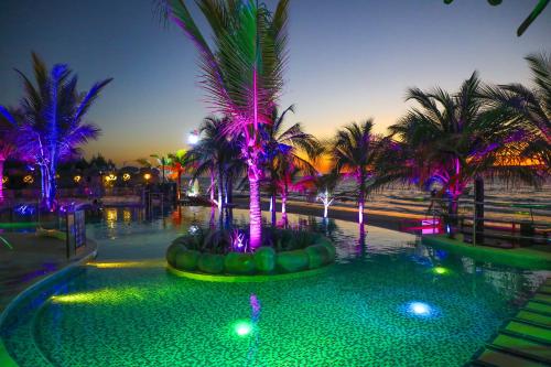 a pool with palm trees at night with lights at Laguna Beach, Brisa Marina playa Frances in Coveñas