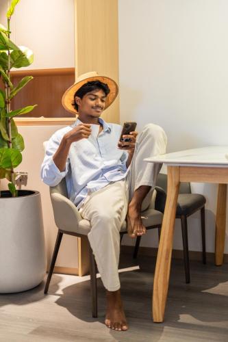 a man wearing a hat sitting in a chair looking at his cell phone at Lazzlla Beachfront Oceanfront Apartments in Hulhumale