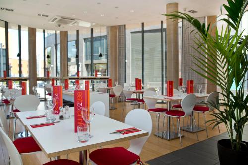 a restaurant with white tables and red chairs at Sleeperz Hotel Cardiff in Cardiff