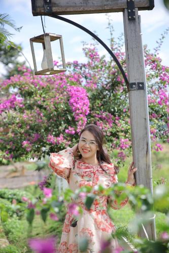 a woman in a dress standing next to a pole with flowers at Upes Garden Homestay Bien Ho in Bien Ho
