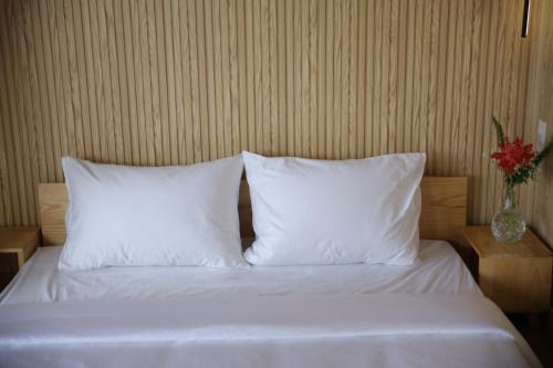 a bed with white pillows and a vase with a flower at Upes Garden Homestay Bien Ho in Bien Ho