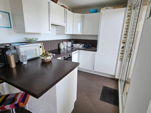 une cuisine avec des armoires blanches et un comptoir noir dans l'établissement Appartement 3 chambres proche mer, terrasse sud - FR-1-768-120, à La Garonnette-Plage