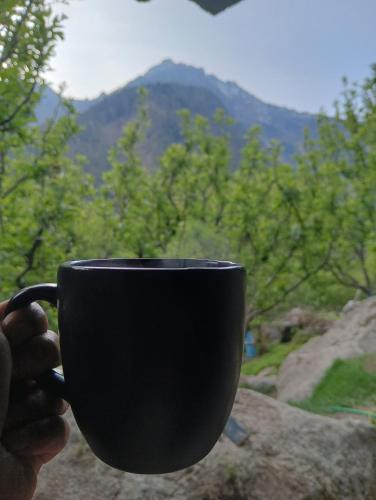 a person holding a black coffee cup with a mountain at Harsil woodstone homestay in Harsil
