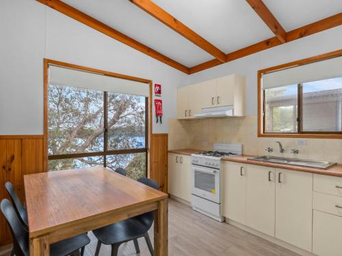 a kitchen with white cabinets and a table with chairs at Joalah Holiday Park in Durras