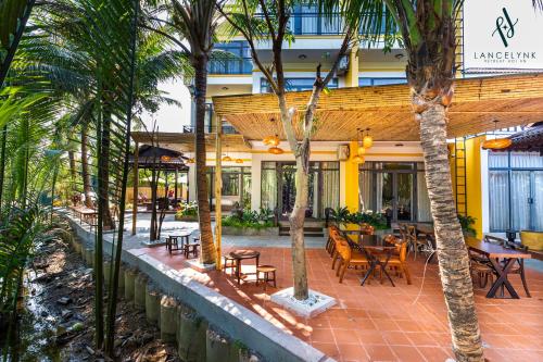 a courtyard with tables and chairs and palm trees at Lancelynk Retreat Hoi An in Hoi An