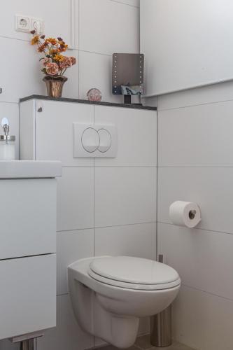 a white bathroom with a toilet and a vase of flowers at B&B Het Gelders Buitenleven in Overasselt