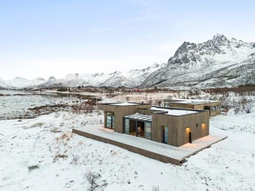 a house in the snow with mountains in the background at Lofoten Seafront Lodge, Lyngvær in Lyngværet