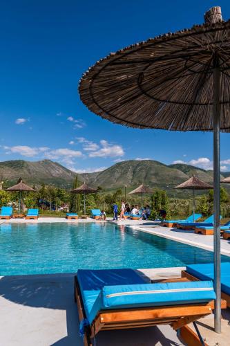 a pool with an umbrella and chairs and people in the water at Mesopotam Agrotourism Resort in Sarandë