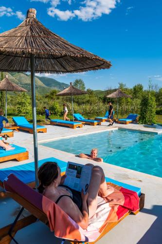 a woman laying on a lounge chair with a laptop next to a swimming pool at Mesopotam Agrotourism Resort in Sarandë