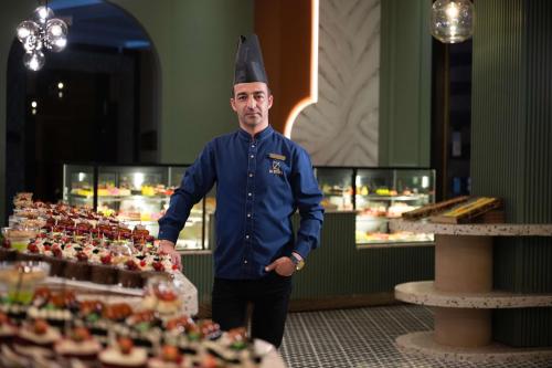 a man in a chef hat standing next to a display of food at Oz Hotels Sui in Alanya