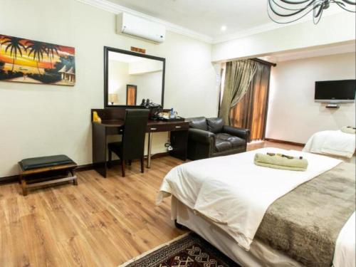 a hotel room with a bed and a desk and a mirror at Royl Court Guesthouse in Kimberley