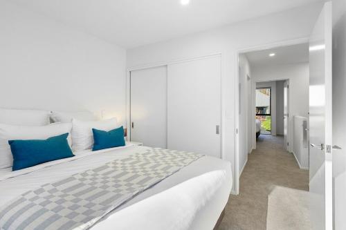 a white bedroom with a large bed with blue pillows at Stylish Stay Heart of the CBD in Christchurch