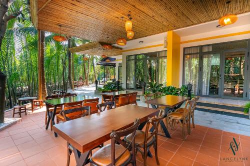 a restaurant with wooden tables and chairs and windows at Lancelynk Retreat Hoi An in Hoi An