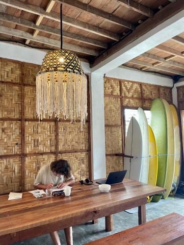 a woman sitting at a wooden table with a laptop at Sun & Surf Hostel - STARLINK in Santa Monica