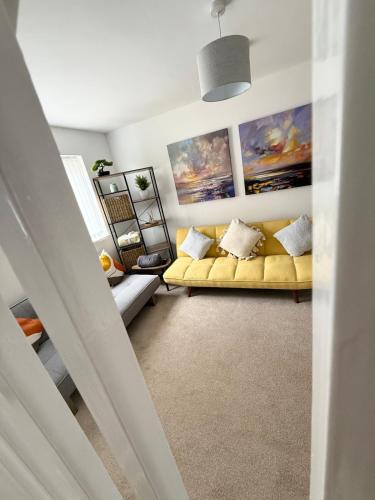a living room with a yellow couch and paintings at Lovely 2 Bed End Terrace - Private Parking - Garden in Cardiff