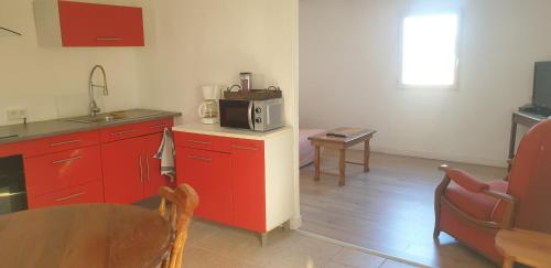 La cuisine est équipée de placards rouges, d'une table et d'un four micro-ondes. dans l'établissement Petite maison avec jardinet, à Revest-du-Bion