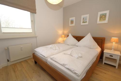 a bedroom with a bed with white sheets and a window at Entennest am Dorfteich in Wenningstedt