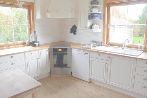 una cocina con armarios blancos, fregadero y ventanas en Between the dunes and the sea, en Les Moitiers-dʼAllonne