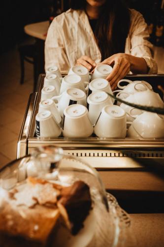 a woman sitting in front of a group of white cups at Pensjonat Witoldówka in Krynica Zdrój