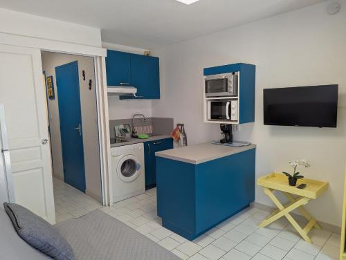 une petite cuisine avec des armoires bleues et un lave-linge dans l'établissement Sol-y-Days Floralies, Studio grande terrasse résidence avec piscine, au Grau-du-Roi