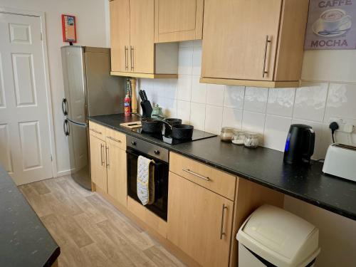 a kitchen with wooden cabinets and a black counter top at Ideal 2 bed pay-as-you-stay home in Widnes sleeps 5 in Halton