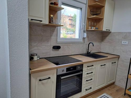Una cocina con gabinetes blancos y un fregadero y una ventana. en MIL apartment Sokobanja, en Soko Banja