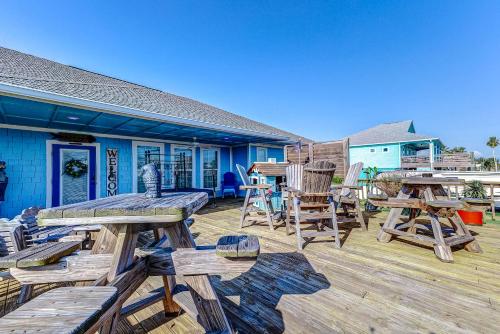 a deck with wooden tables and chairs on a house at Blue Heaven by Bolivar Escapes in Crystal Beach