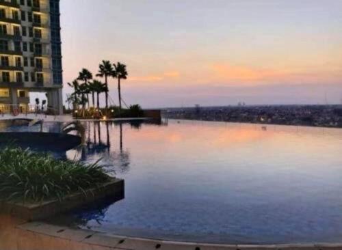 a large pool of water with palm trees and a building at LuxBedAndersonPakuwon by BnB in Surabaya
