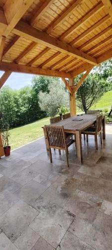 une table et des bancs en bois sous un toit en bois dans l'établissement Maison de vacances en Périgord, à Fleurac