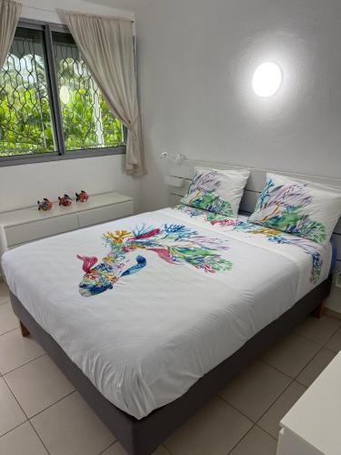 a bed with a white comforter with a dragon on it at COMME un POISSON in Sainte-Anne