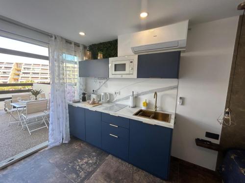 une cuisine avec des armoires bleues, un évier et une fenêtre dans l'établissement LA SUITE DES CHARMES - village naturiste - coursives - port nature 2, au Cap d'Agde