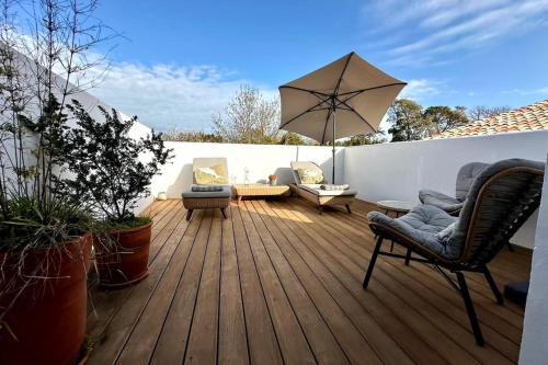 une terrasse en bois avec des chaises et un parasol dans l'établissement The Lighthouse Quiet terrace apartment on the port, à Saint-Martin-de-Ré
