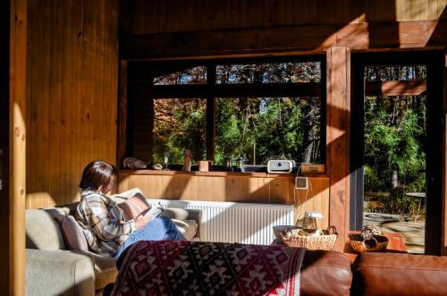 a woman sitting on a couch looking out a window at Refugios Australes en Corralco in Malalcahuello
