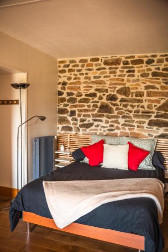 - une chambre dotée d'un mur en pierre et d'un lit avec des oreillers rouges dans l'établissement Lodge de La Vallée, à Saint-Rémy