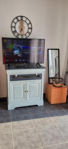 a tv on a stand with a clock on the wall at Appartement 2-3 personnes Saint Cast le Guildo in Saint-Cast-le-Guildo