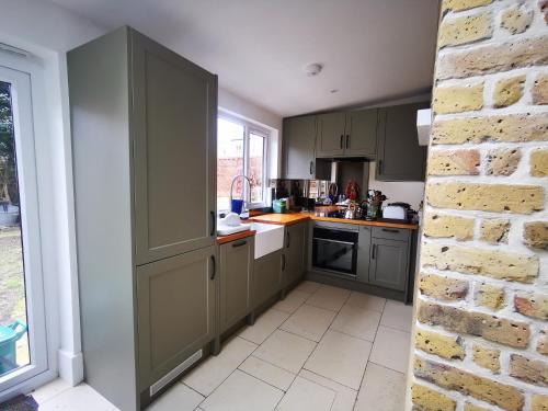 a kitchen with green cabinets and a brick wall at The Cozy Nest - West London in Brentford