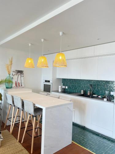 une cuisine avec des placards blancs et un îlot avec des tabourets de bar dans l'établissement Les pieds dans le sable, à La Baule