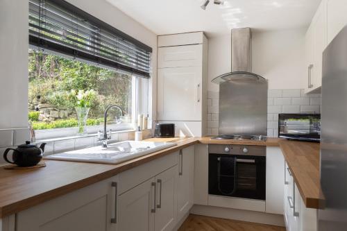 eine Küche mit weißen Schränken und einer Spüle und einem Fenster in der Unterkunft 'Haworth Haven', Warm Winter Cottage Getaway in Haworth