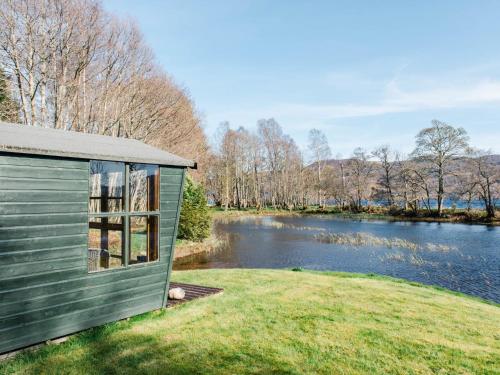 a green house on a lawn next to a river at Holiday Home Farmburn Bothy by Interhome in Invermoriston